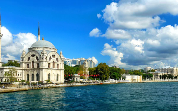 A stunning HD wallpaper of Istanbul, featuring a beautifully designed building along the waterfront, framed by vibrant blue skies and fluffy clouds.