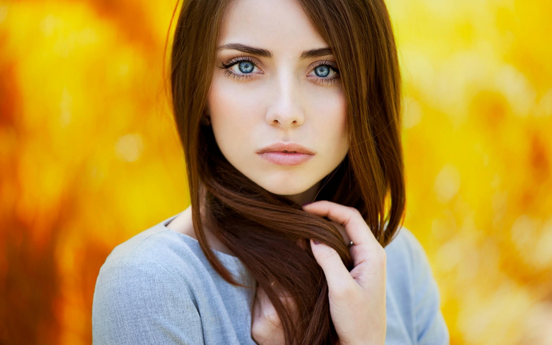 A striking HD wallpaper featuring a model with long hair and captivating blue eyes, set against a warm, golden background.