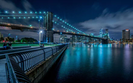 HD desktop wallpaper: Brooklyn Bridge at night, blue lights tracing suspension cables, reflected in the East River with New York skyline under a deep blue sky.