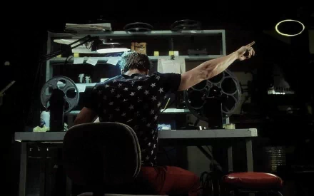 A HD desktop wallpaper and background from the movie Fight Club, featuring a character pointing at the ceiling while sitting at a cluttered desk in a dark room.