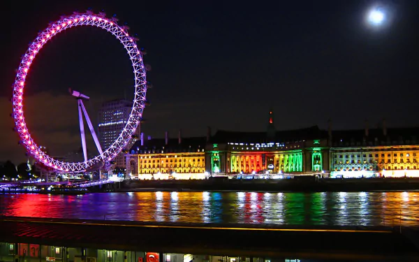 Night view of the man-made London Eye ferris wheel glowing pink beside rainbow-lit riverside buildings, moon over the Thames and colorful reflections, 2K Quad HD PC desktop wallpaper.