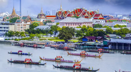 2K Quad HD wallpaper: Bangkok's man-made Grand Palace along the Chao Phraya River, colorful longboats and riverside houses under a blue sky.