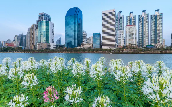 View of Bangkok's modern skyline along the Chao Phraya River with vibrant flowers in the foreground, showcasing Thailand’s urban and natural beauty.