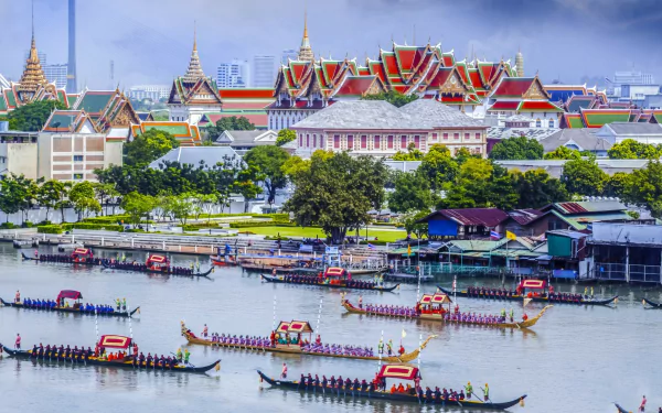 2K Quad HD wallpaper: Bangkok's man-made Grand Palace along the Chao Phraya River, colorful longboats and riverside houses under a blue sky.