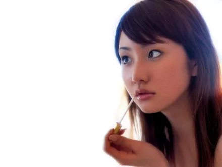 An Asian woman with long hair engages in a sensual moment, holding a lip gloss wand. The soft background creates a serene atmosphere, making this an elegant HD desktop wallpaper.