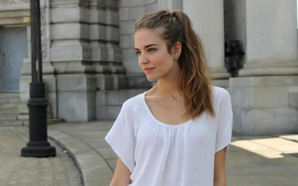 A Spanish woman, Clara Alonso, poses gracefully outdoors, wearing a white top against a scenic backdrop, creating an engaging HD desktop wallpaper.
