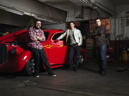 HD wallpaper of three men from Top Gear standing beside a red classic car in a garage.