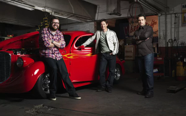 HD wallpaper of three men from Top Gear standing beside a red classic car in a garage.