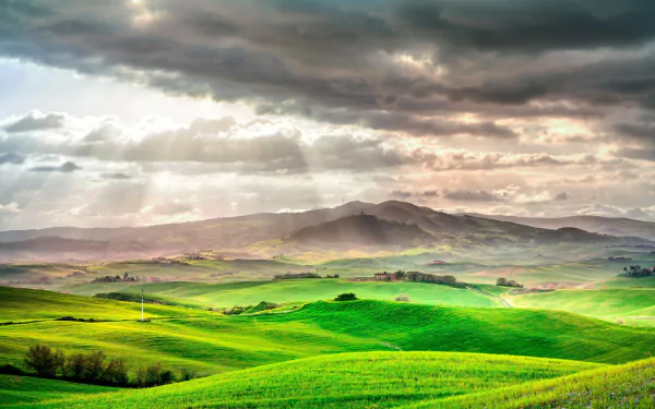 Sunlit rolling fields of Tuscany, Italy under dramatic clouds, captured in vibrant HD for a stunning desktop wallpaper background.