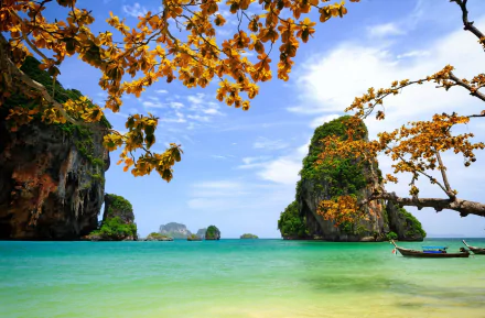 Tropical Thailand seascape photography: turquoise sea, limestone karsts and a longtail boat framed by golden foliage under blue sky — HD PC desktop wallpaper/background.