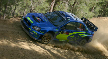Blue Subaru Impreza WRC rally car kicking up dust on a forest dirt stage — dynamic 2K Quad HD PC desktop wallpaper and background.