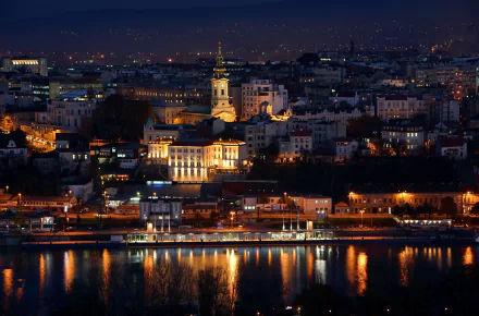 Night view of Belgrade cityscape along the Danube River in Serbia, showcasing illuminated historic buildings and waterfront reflections in this HD desktop wallpaper.