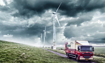 A DAF vehicle drives on a road beside wind turbines under dramatic cloud-filled skies in the Netherlands, captured in 4K Ultra HD.