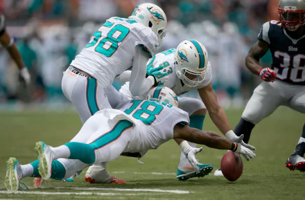 HD PC desktop wallpaper featuring Miami Dolphins players in white uniforms recovering a fumble during a football game, capturing dynamic sports action.