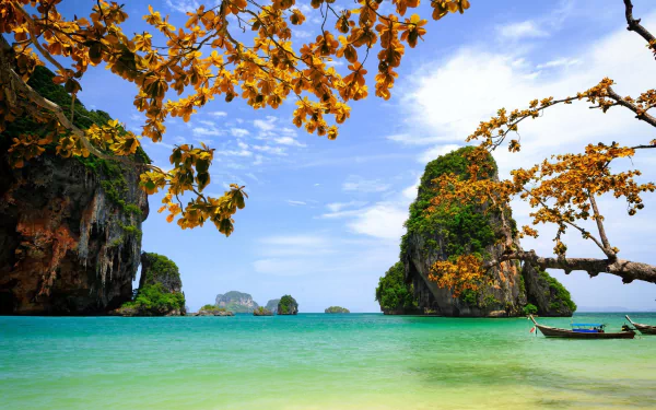 Tropical Thailand seascape photography: turquoise sea, limestone karsts and a longtail boat framed by golden foliage under blue sky — HD PC desktop wallpaper/background.