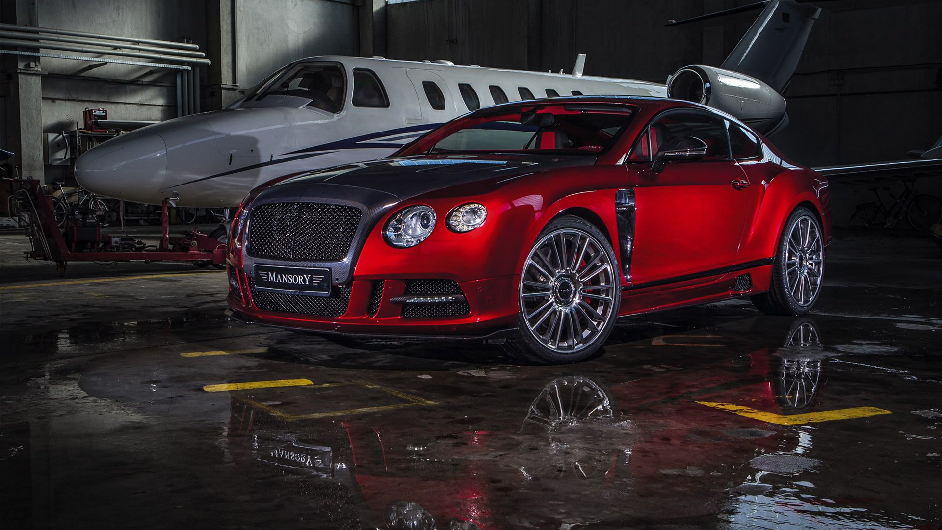Red Bentley Continental vehicle parked in a dim hangar beside a private jet, glossy wet-floor reflection — HD PC desktop wallpaper background.