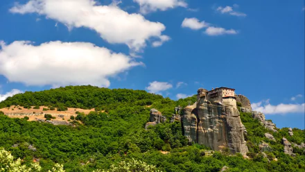 HD desktop wallpaper of Meteora's religious monasteries perched atop towering rock formations under a bright blue sky with scattered clouds.