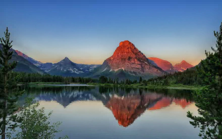 Sunrise over Sinopah Mountain reflecting in Pray Lake at Glacier National Park, Montana, with clear skies and calm water capturing the serene dawn landscape.