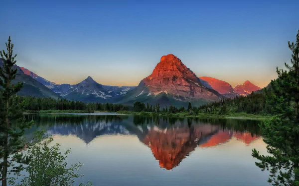 Sunrise over Sinopah Mountain reflecting in Pray Lake at Glacier National Park, Montana, with clear skies and calm water capturing the serene dawn landscape.