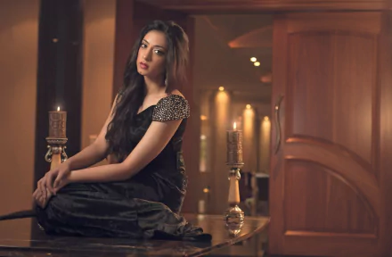 A woman in a black dress sits gracefully on a table in an elegantly lit room, creating a stylish HD desktop wallpaper and background.