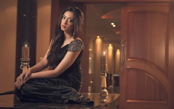 A woman in a black dress sits gracefully on a table in an elegantly lit room, creating a stylish HD desktop wallpaper and background.