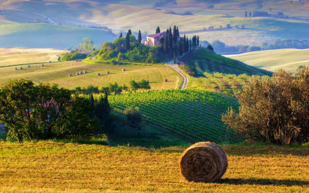 Scenic HD desktop wallpaper of a Tuscany villa surrounded by rolling hills, haystacks, and lush fields in Italy’s countryside.