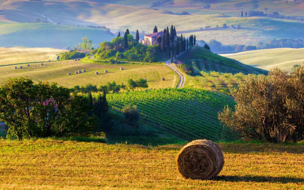 Scenic HD desktop wallpaper of a Tuscany villa surrounded by rolling hills, haystacks, and lush fields in Italy’s countryside.