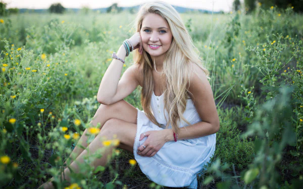 HD desktop wallpaper featuring a woman with a smile, sitting in a lush green field surrounded by wildflowers.