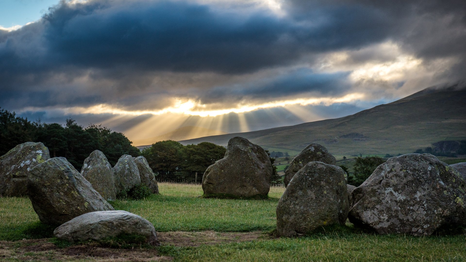 A serene landscape featuring a stunning sunbeam breaking through clouds over ancient stones, showcasing the beauty of nature in vibrant 4K Ultra HD.