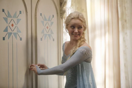 Elsa from the TV show Once Upon A Time stands by a decorated wardrobe, displaying her signature ice blue gown and playful smile in this HD wallpaper background.