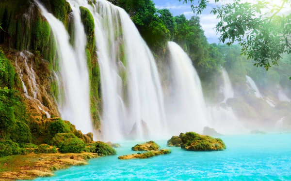 HD desktop wallpaper featuring a stunning nature scene with cascading waterfalls, lush green foliage, and turquoise water under a bright sky.