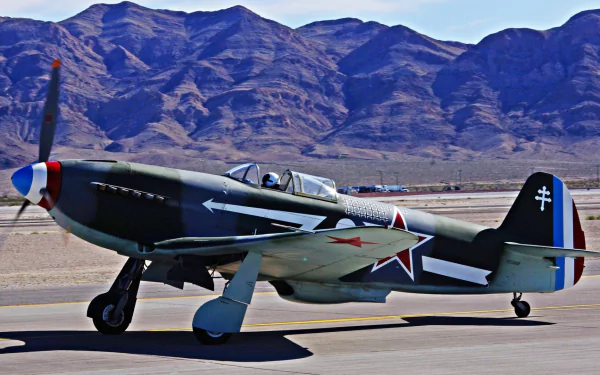 HD PC desktop wallpaper/background showing a military Yakovlev Yak-3 fighter taxiing on a desert runway with rugged mountains in the background.
