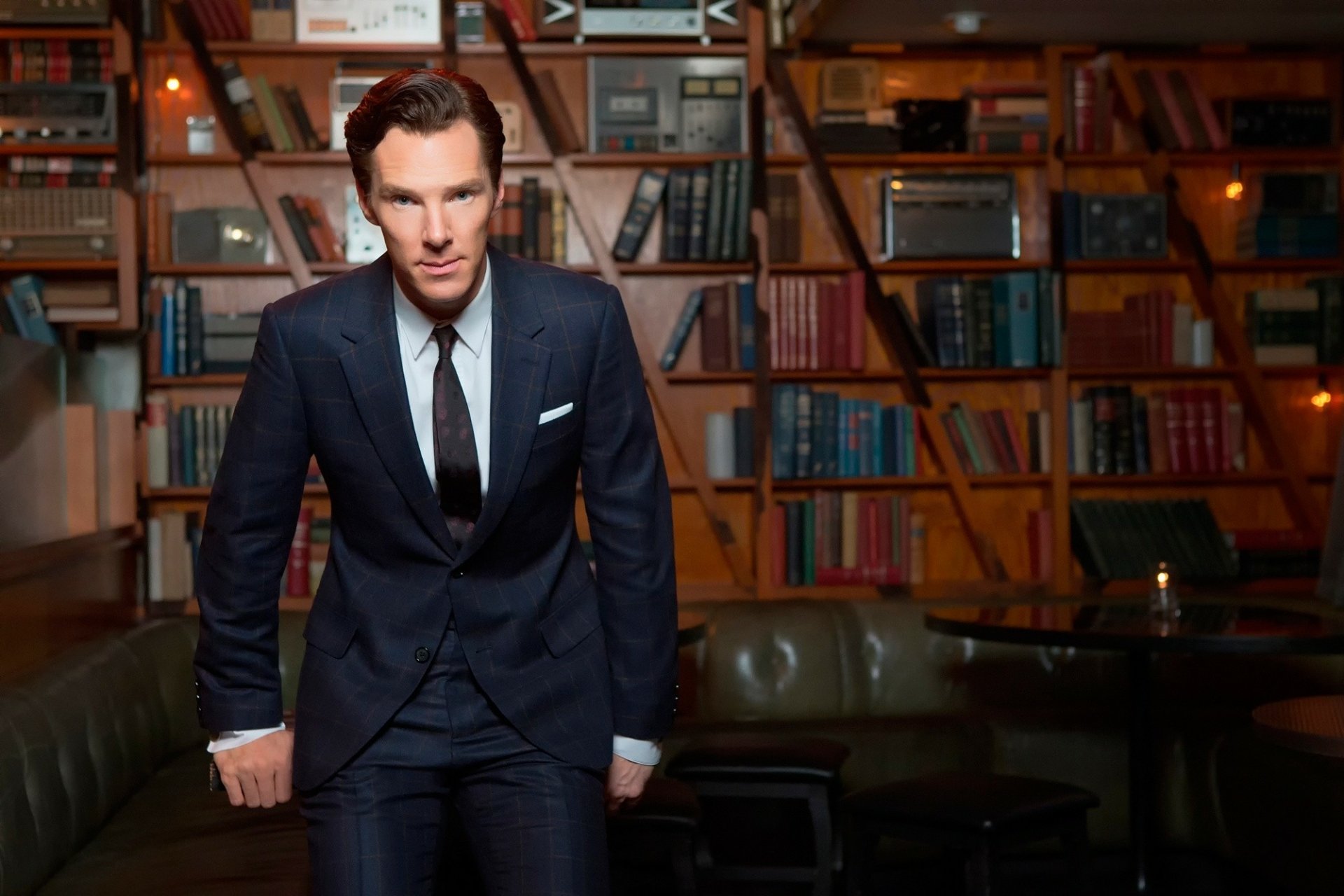 Benedict Cumberbatch as Sherlock Holmes stands confidently in a richly detailed library room, captured in a high-definition PC desktop wallpaper.