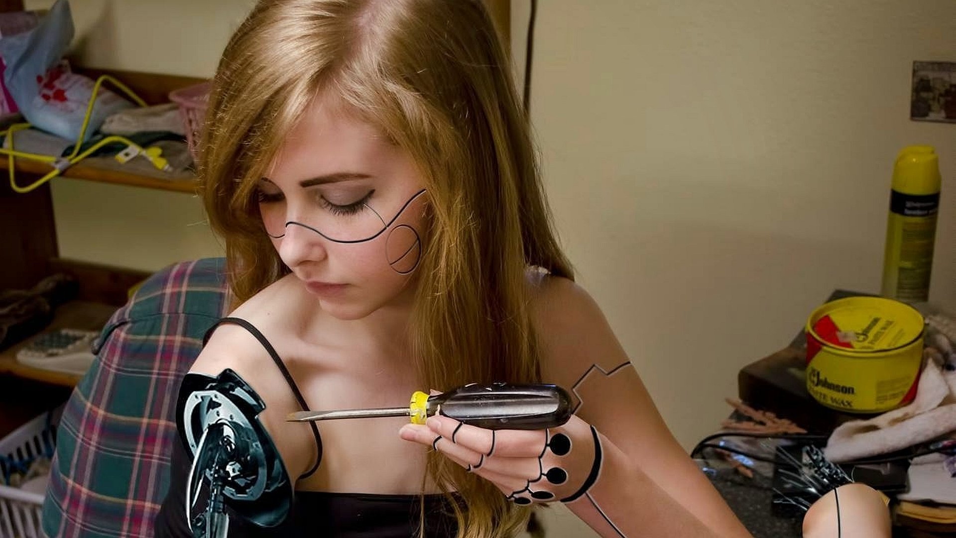 A cyborg woman with mechanical enhancements works intently with a screwdriver, surrounded by tools and wires, creating a futuristic sci-fi atmosphere in this HD desktop wallpaper.