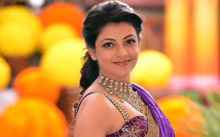 HD wallpaper featuring Indian actress Kajal Aggarwal from the movie Govindudu Andarivadele, dressed in a purple saree and ornate necklace, with a vibrant, colorful background.