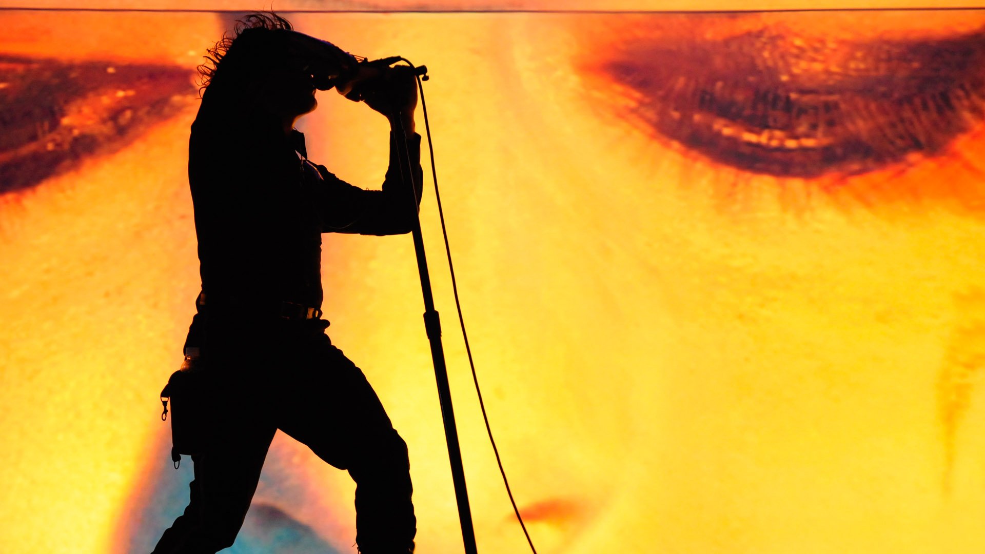 Silhouette of a singer at a microphone stand against a fiery close-up face — HD PC desktop wallpaper for Tool (music).
