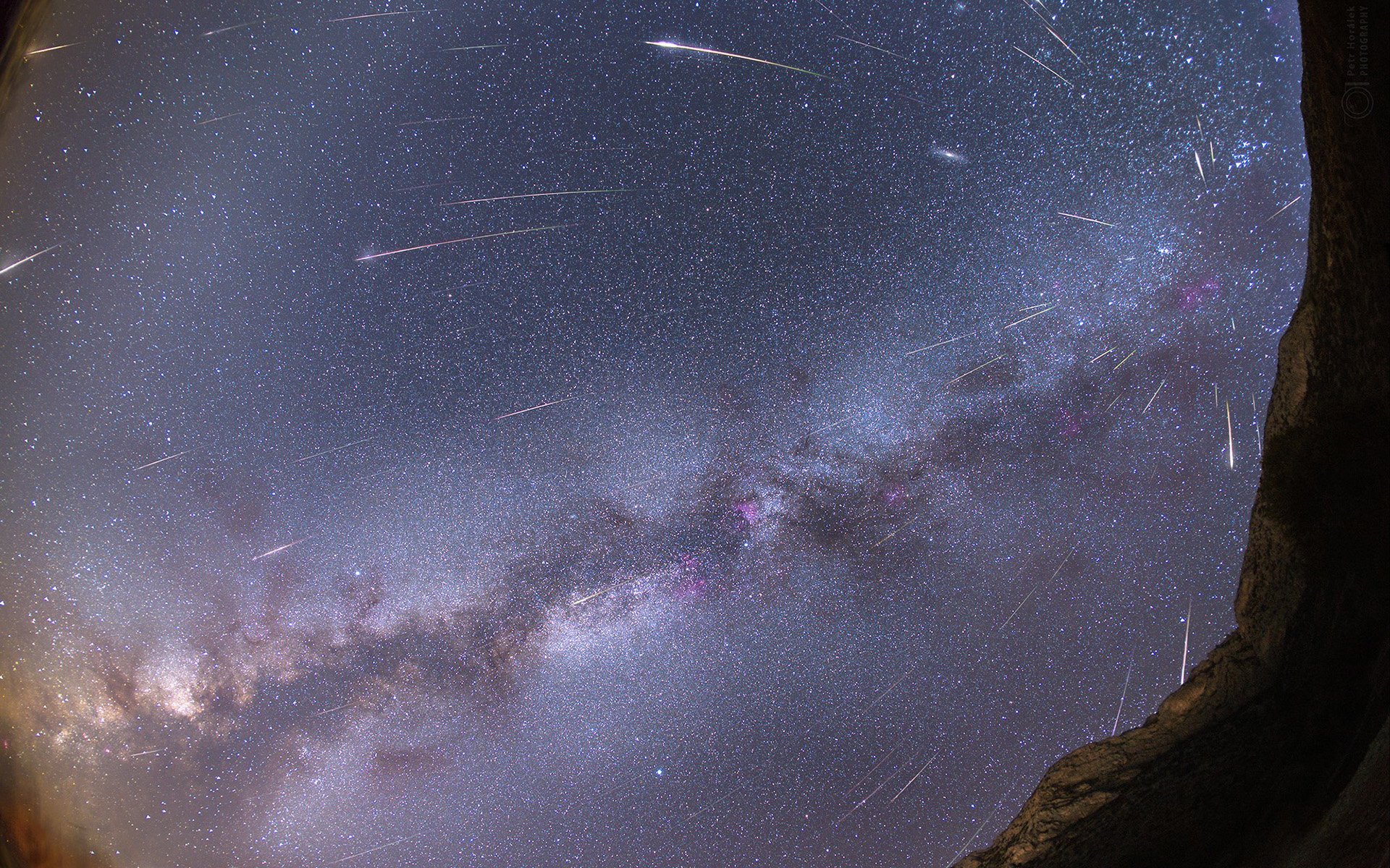 Time-lapse sci-fi starfield with meteor streaks over the Milky Way and a silhouetted rock foreground — HD PC desktop wallpaper/background.