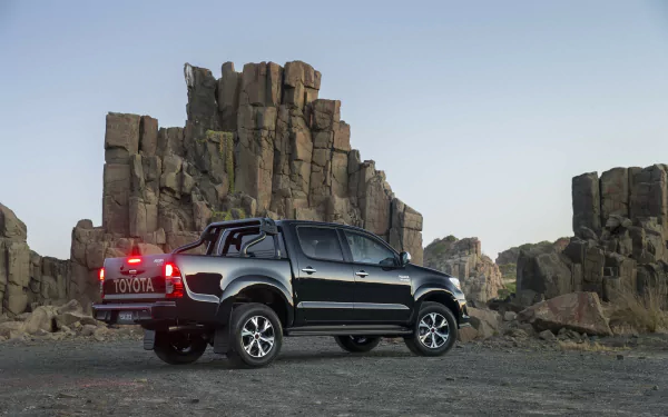 HD desktop wallpaper featuring a black Toyota Hilux parked against rugged rock formations, showcasing the vehicle's robust design in a natural outdoor setting.