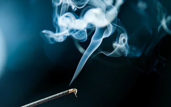 A close-up of smoke swirling gracefully from an incense stick against a dark, blurred background, showcasing a serene and artistic atmosphere. This vivid image is available as a 4K Ultra HD wallpaper.