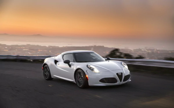 A sleek white Alfa Romeo 4C drives along a coastal road at sunset, with a city skyline in the background, creating a stunning HD desktop wallpaper scene.