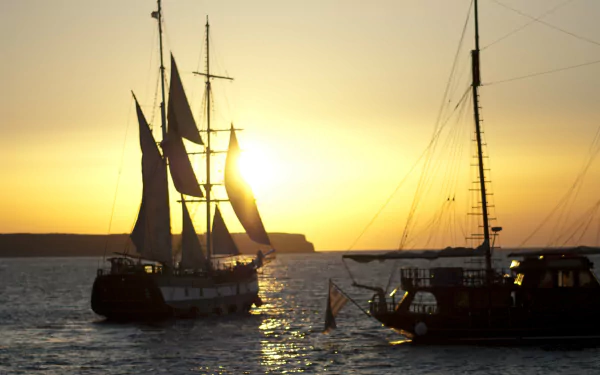 4K Ultra HD PC desktop wallpaper showing two sailing ships (vehicle, ship) silhouetted on calm water at golden sunset.