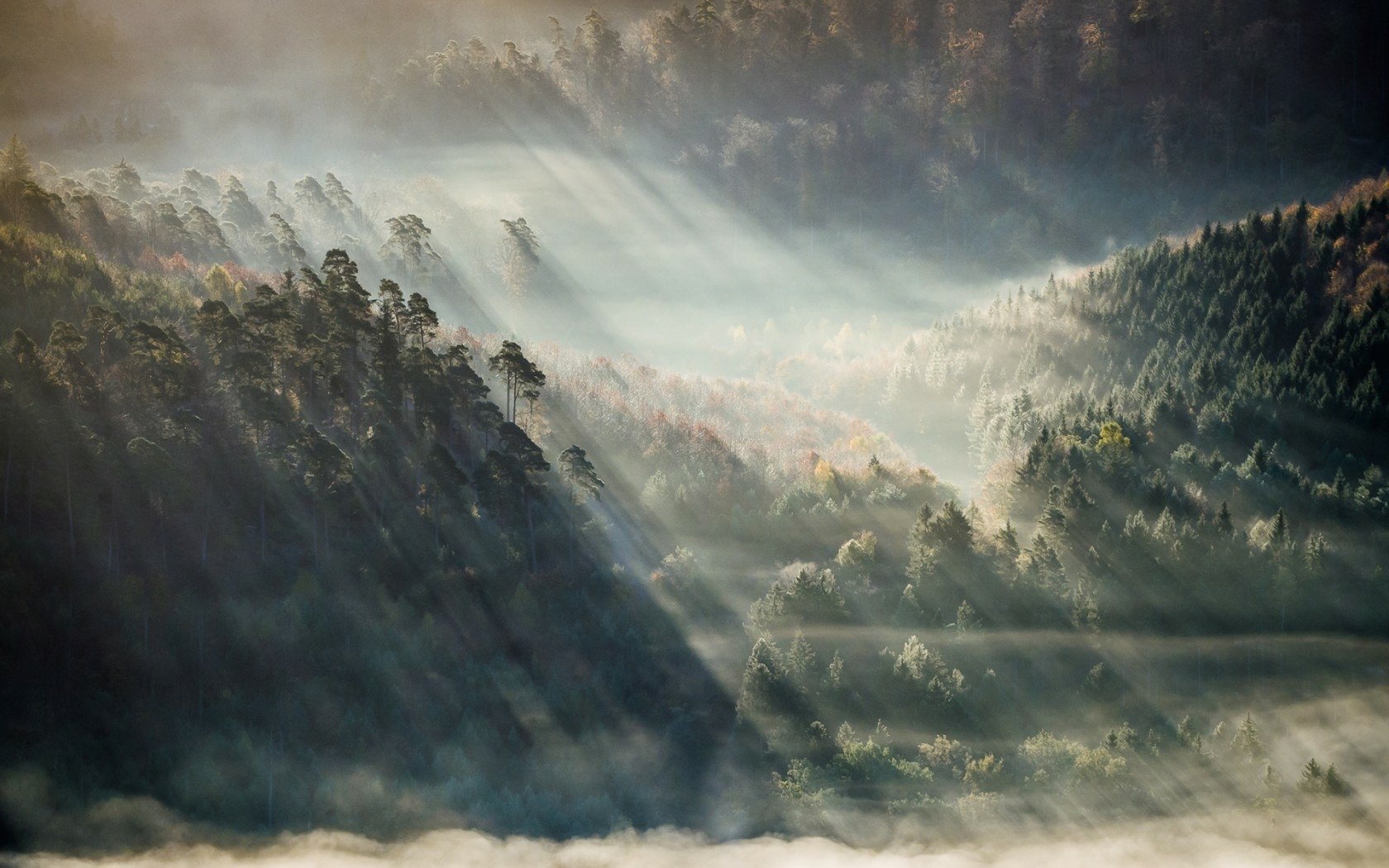 HD PC desktop wallpaper: nature scene with sunbeams piercing morning mist over forested valleys and rolling hills.