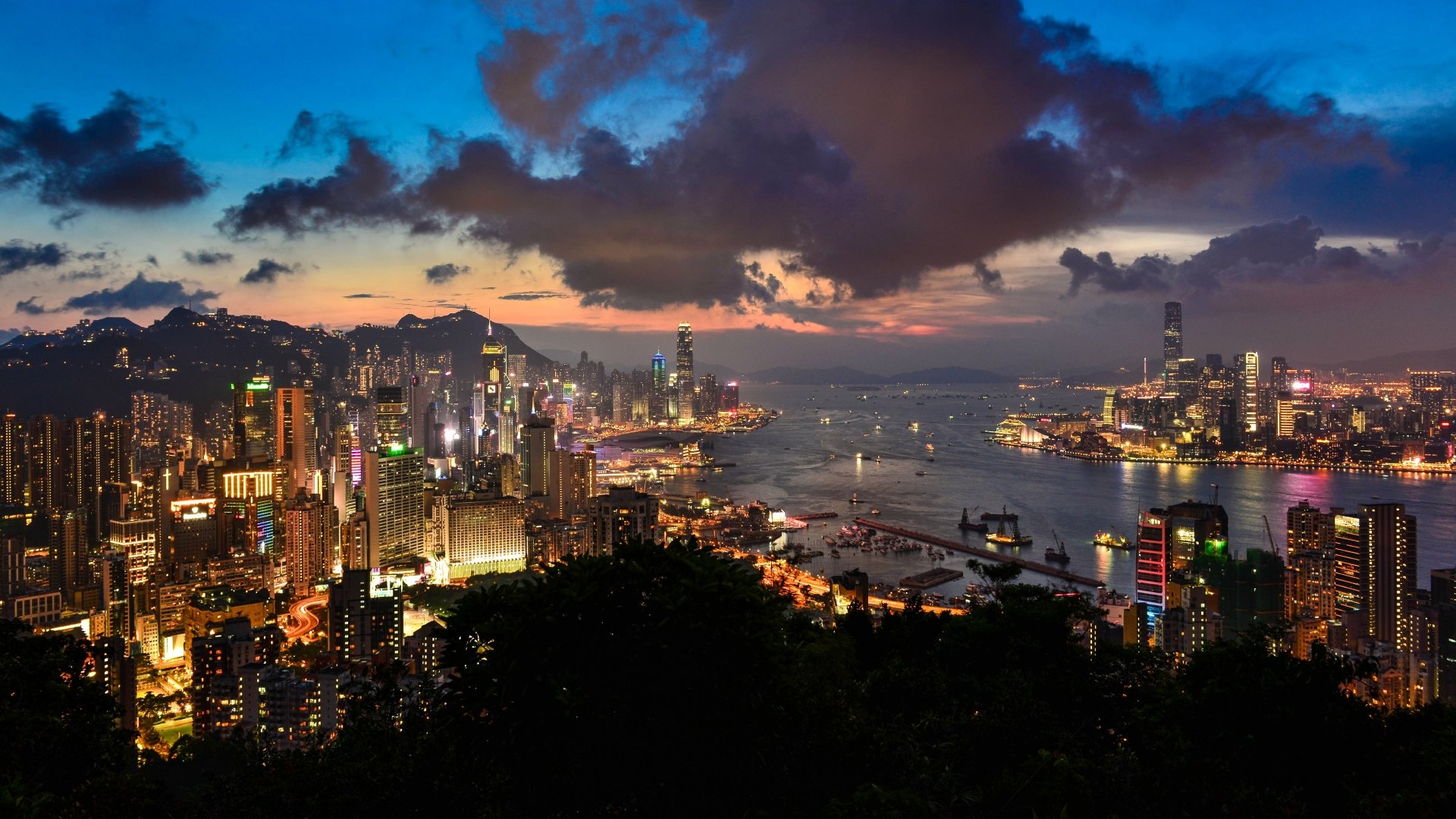 A stunning 4K Ultra HD view of Hong Kong’s skyline at dusk, showcasing towering skyscrapers, the vibrant harbor, and a dramatic cloud-filled sky.
