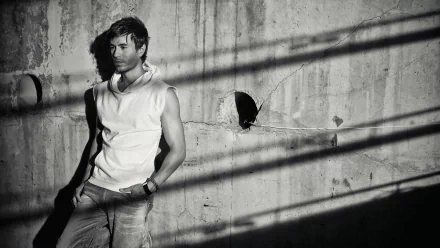 A striking black and white HD wallpaper featuring Enrique Iglesias, standing against a textured concrete wall with dramatic shadows, capturing his confident, artistic persona.