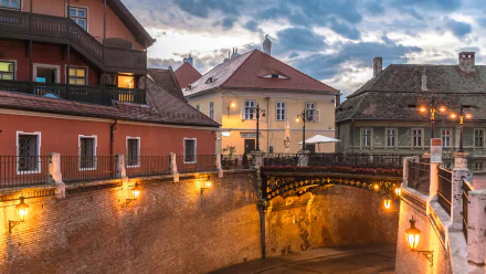4K Ultra HD PC desktop wallpaper of Sibiu streets: historic man-made stone bridge and illuminated old town buildings under a moody evening sky