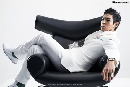 A member of Bigbang dressed in white, reclining confidently on a modern black chair; a 4K Ultra HD music-themed PC desktop wallpaper.