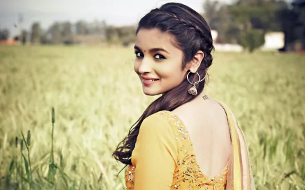 HD desktop wallpaper of Alia Bhatt from the Bollywood movie Humpty Sharma Ki Dulhania, featuring her in a field, wearing a yellow traditional outfit and looking over her shoulder with a smile.
