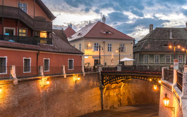 4K Ultra HD PC desktop wallpaper of Sibiu streets: historic man-made stone bridge and illuminated old town buildings under a moody evening sky