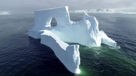 HD PC desktop wallpaper of a majestic iceberg featuring natural arches floating in calm ocean waters under a cloudy sky.