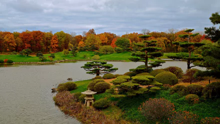 HD PC desktop wallpaper featuring a man-made Japanese garden with sculpted trees, a tranquil pond, and vibrant autumn foliage under a cloudy sky.